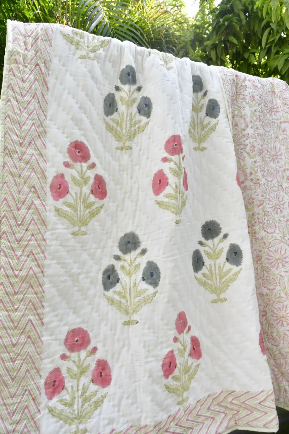 Floral patterned quilt with pink and green flowers on a white background, outdoors.