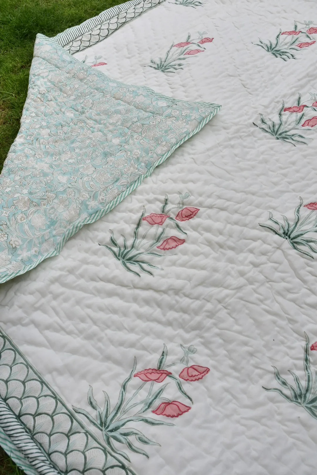 Floral quilt with pink flowers and green leaves on a white background.