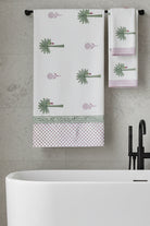 A white cotton tablecloth and matching napkins featuring a green palm tree print, pink polka dot borders, and a decorative green patterned band.