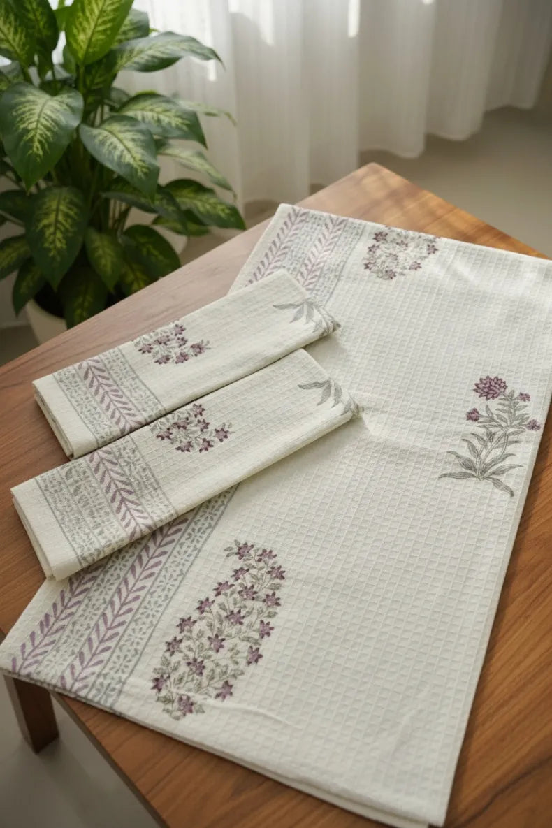Set of embroidered table runner and napkins on a wooden table with a plant in the background.