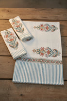 A set of white cotton kitchen towels with blue stripes and orange floral block prints, arranged on a rustic wooden table.
