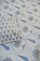 A close-up of a white bedsheet featuring a printed sheet and matching pillowcase with a blue and gray palm tree and leaf pattern.