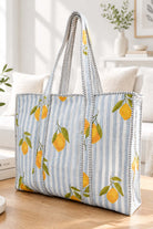 A tote bag with a light blue and white striped fabric body, decorated with yellow lemons and green leaves, featuring black and white striped handles, set on a wooden table in a bright living room.