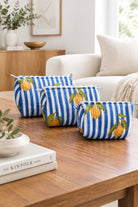 Three zippered cosmetic pouches with a blue and white striped pattern and orange lemon print, arranged on a wooden table in a bright living room setting.