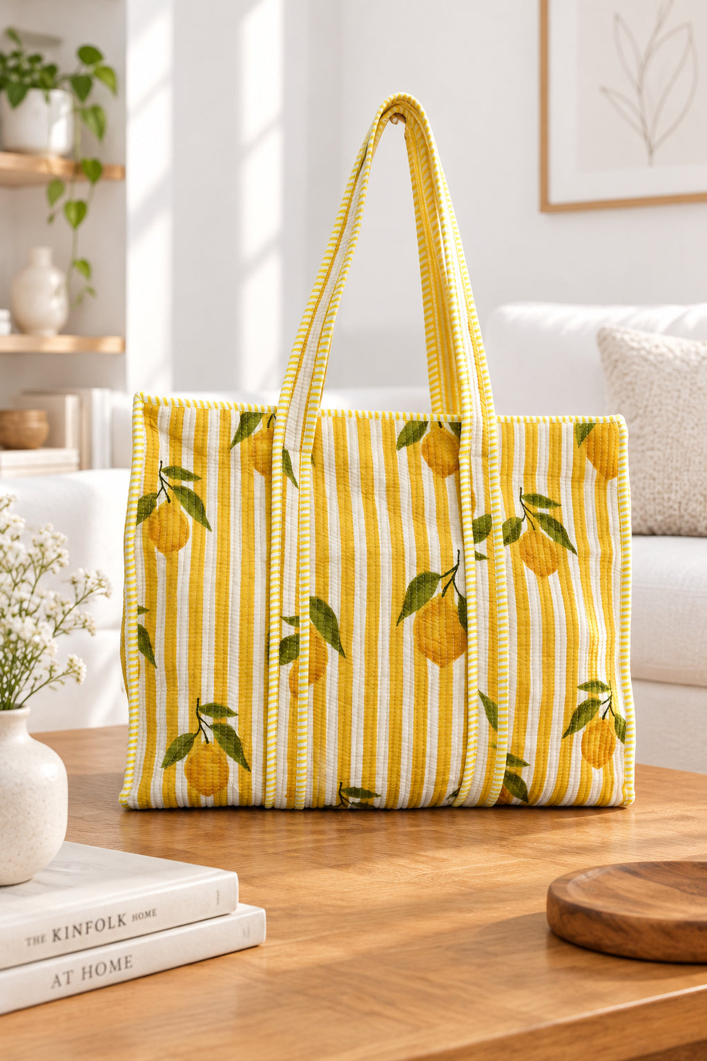 A yellow and white striped tote bag with a lemon print, displayed on a wooden table in a bright, modern living room setting.