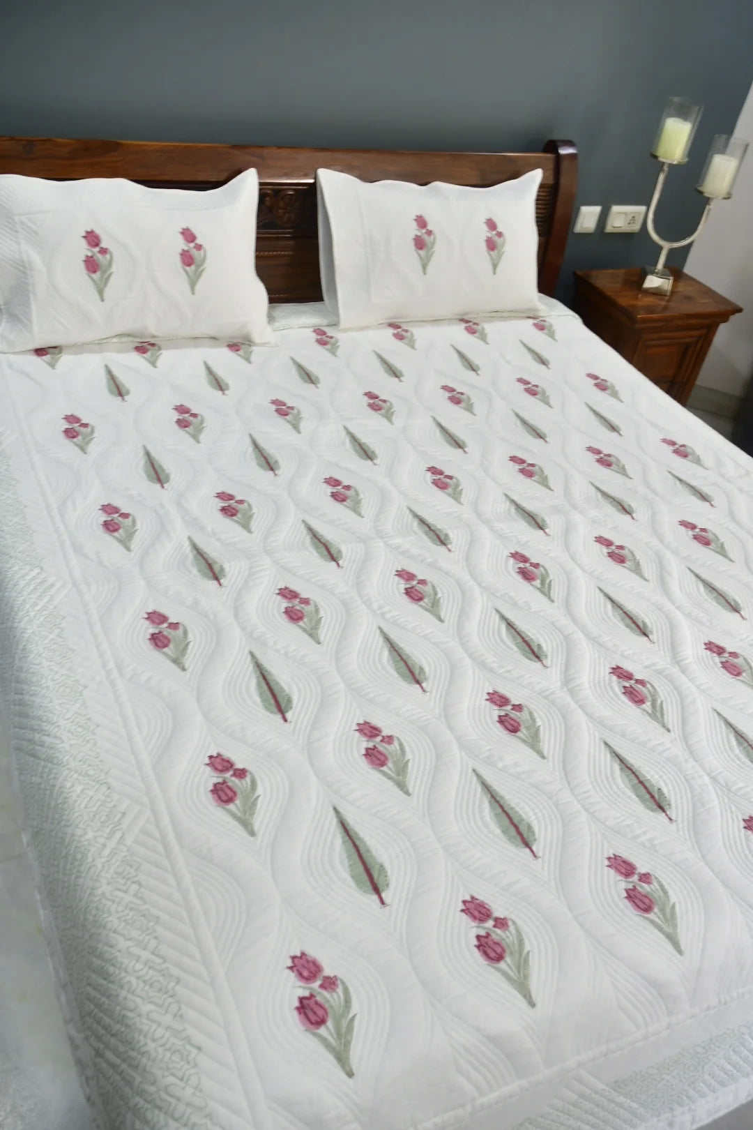 White quilt with floral patterns on a bed in a bedroom setting.