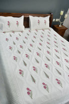 White quilt with floral patterns on a bed in a bedroom setting.