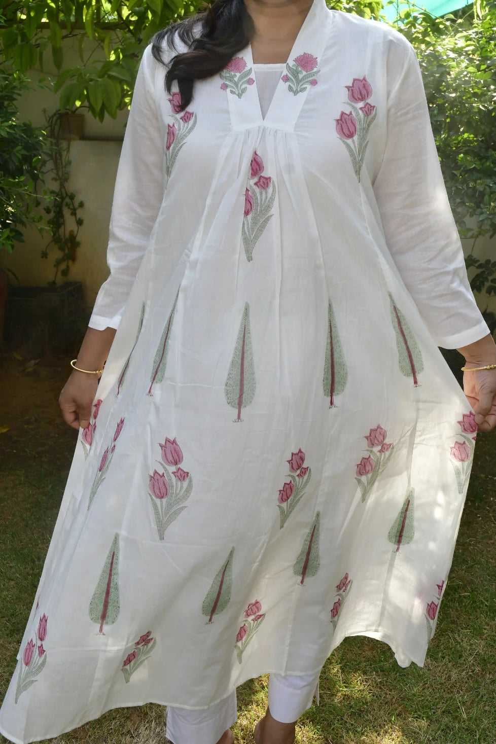 Woman wearing a white embroidered dress with pink flowers outdoors.