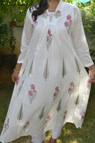 Woman wearing a white embroidered dress with pink flowers outdoors.