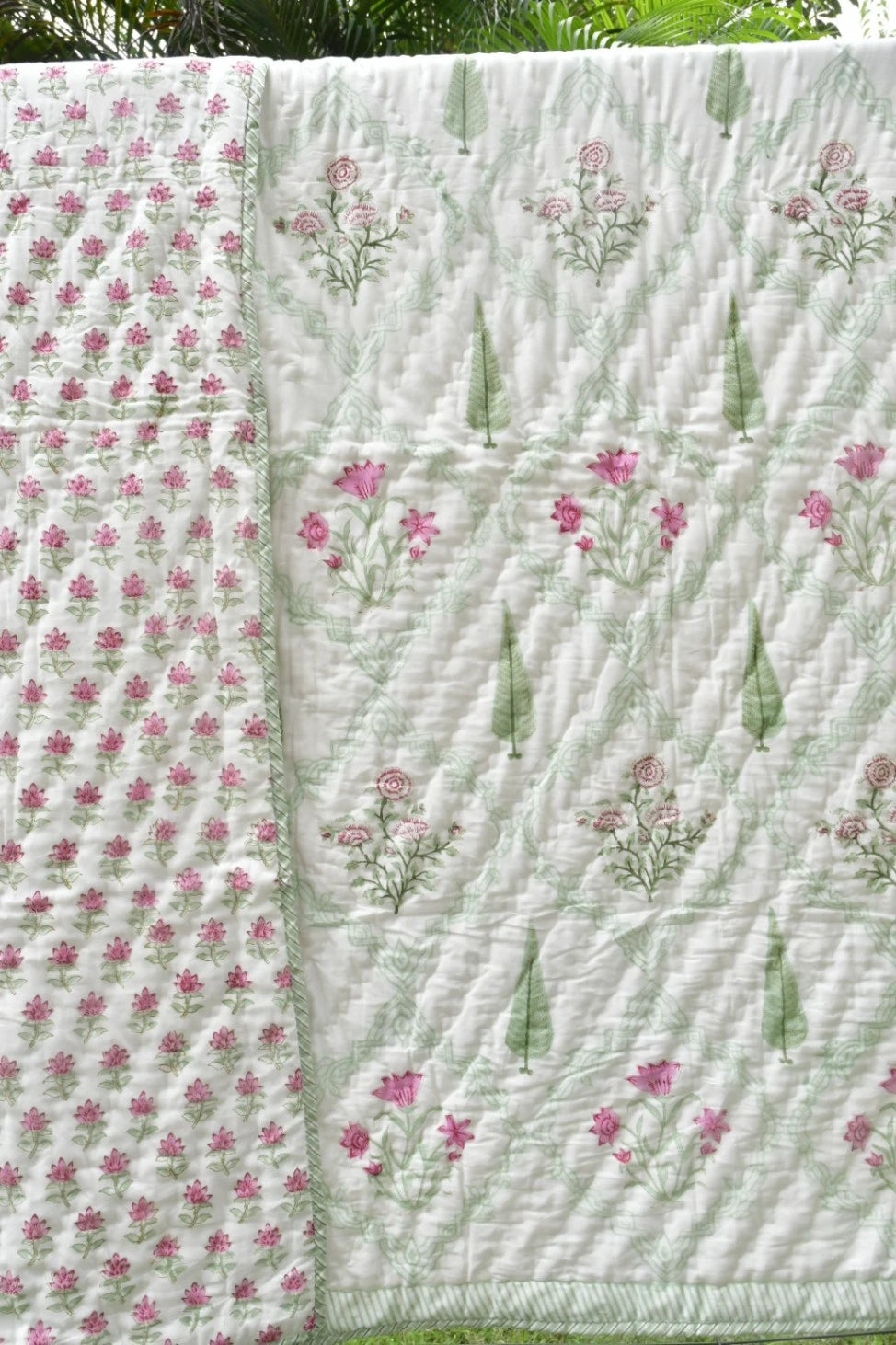 A handmade quilted cotton blanket with a light green and white background, featuring pink floral prints and green leaf motifs, laid out outdoors.
