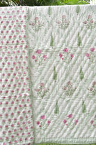 A handmade quilted cotton blanket with a light green and white background, featuring pink floral prints and green leaf motifs, laid out outdoors.