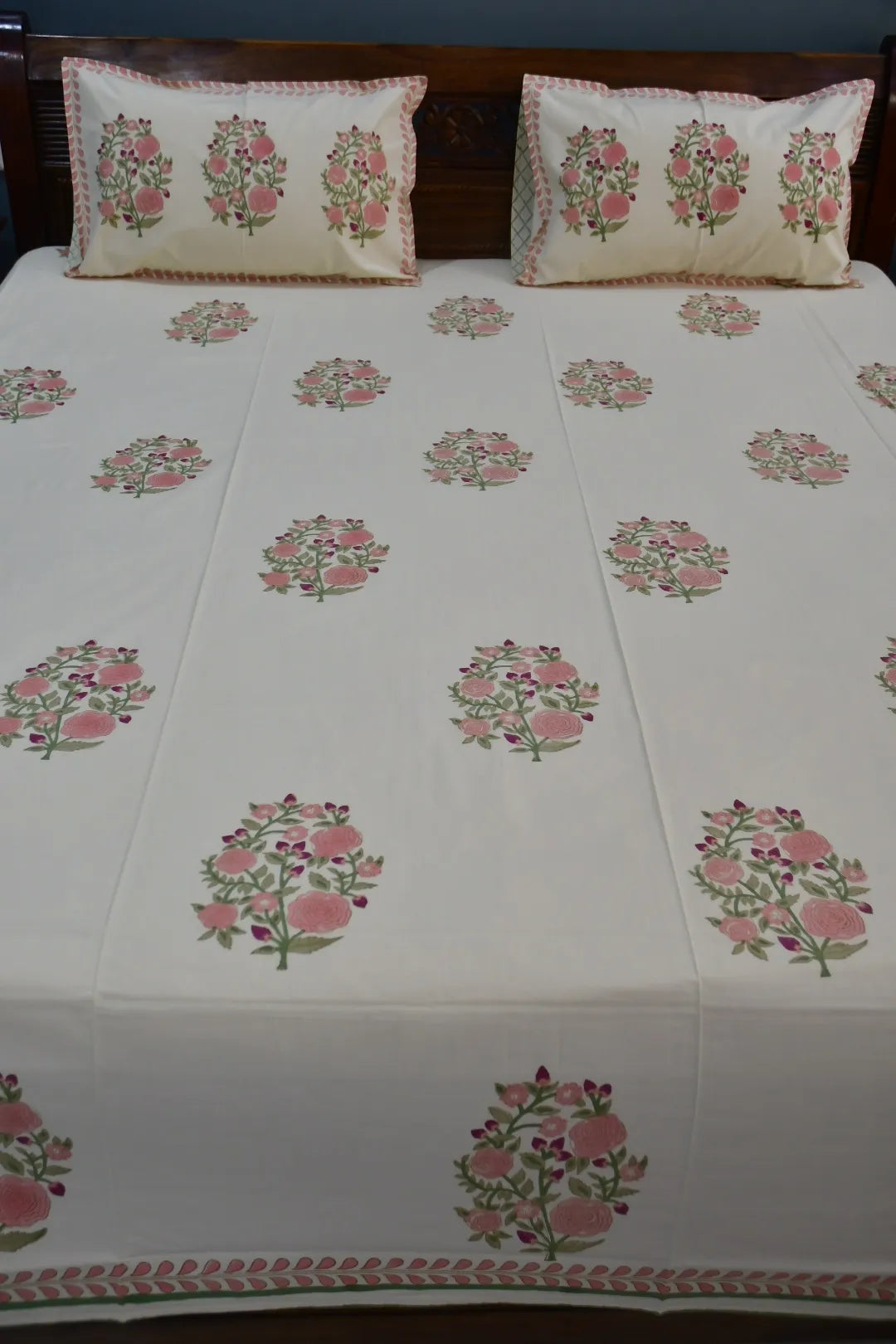 Floral patterned bedding with matching pillows on a wooden bed.