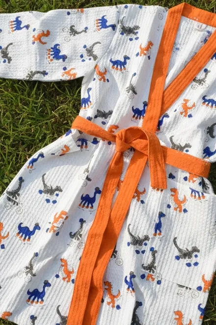 White robe with orange trim and dinosaur pattern on grass