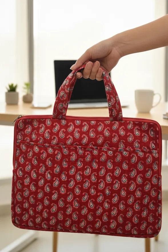 Red patterned laptop bag held by a hand with a blurred indoor background