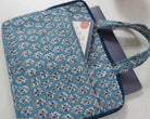 Blue floral-patterned bag on a white surface with a small plant in the background