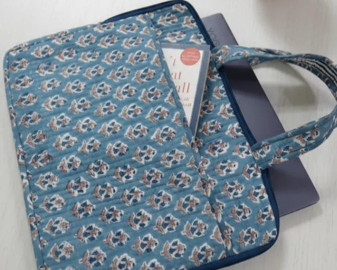 Blue floral-patterned bag on a white surface with a small plant in the background
