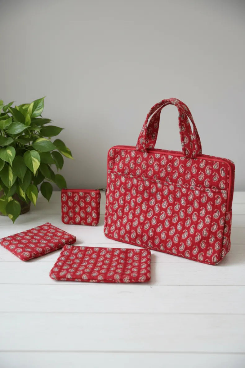 Red patterned bag, pouches, and coaster on a white surface with a plant in the background