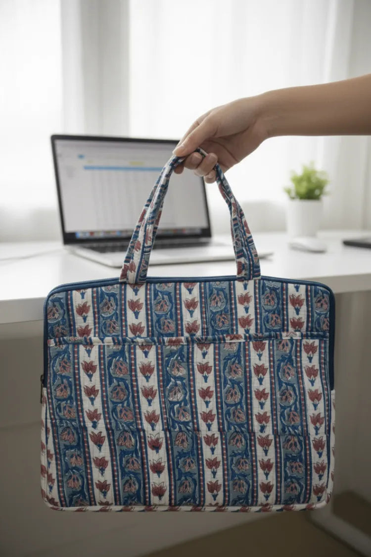Hand holding a patterned bag over a desk with a laptop