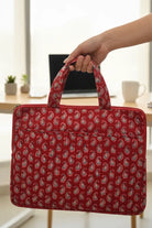 Red patterned laptop bag held by a hand with a blurred indoor background