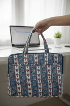 Hand holding a patterned bag over a desk with a laptop