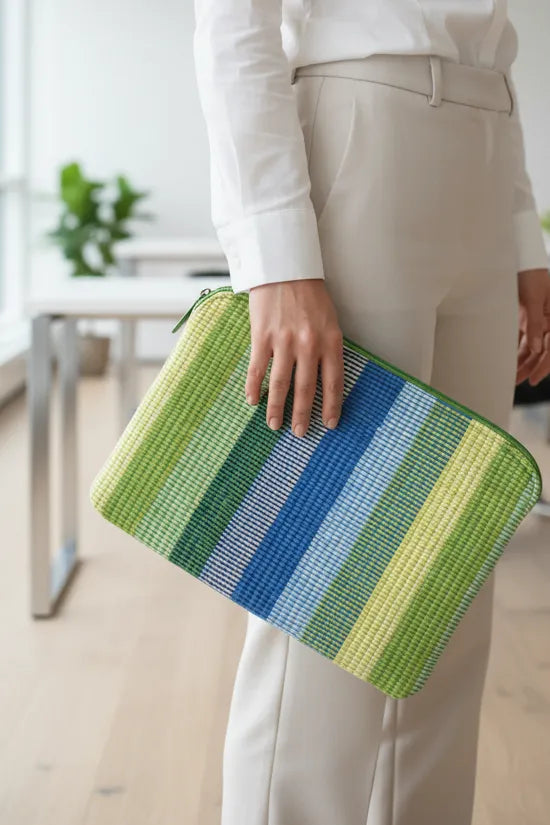 Person holding a green and blue striped laptop sleeve bag office setup.