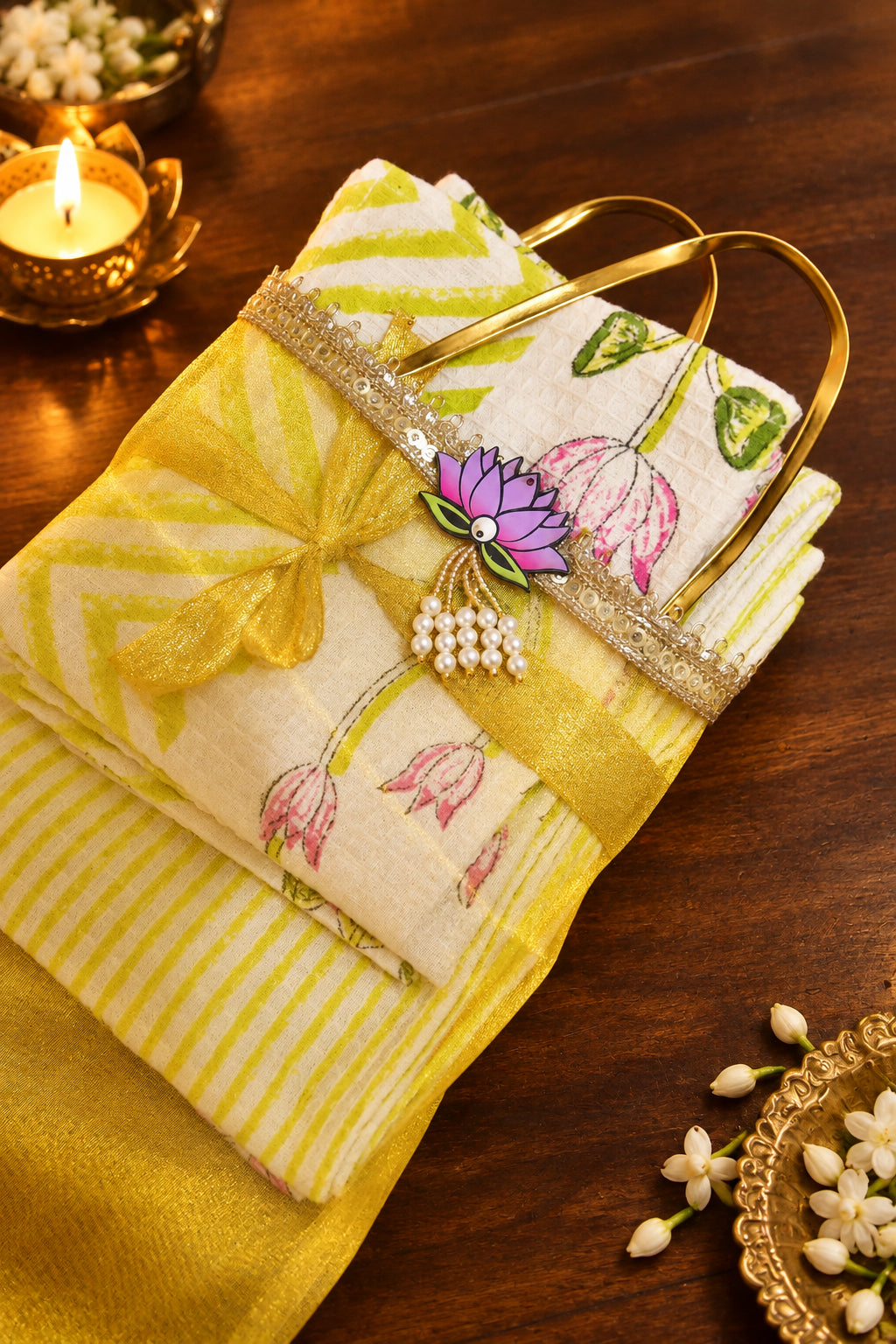 A folded yellow and white striped fabric item with a floral print, tied with a yellow ribbon and decorated with a small flower charm, resting on a dark wooden surface.