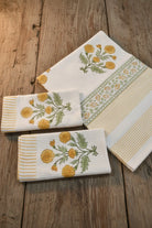 Three white waffle-weave kitchen towels with yellow floral and green leaf embroidery, arranged on a rustic wooden surface.