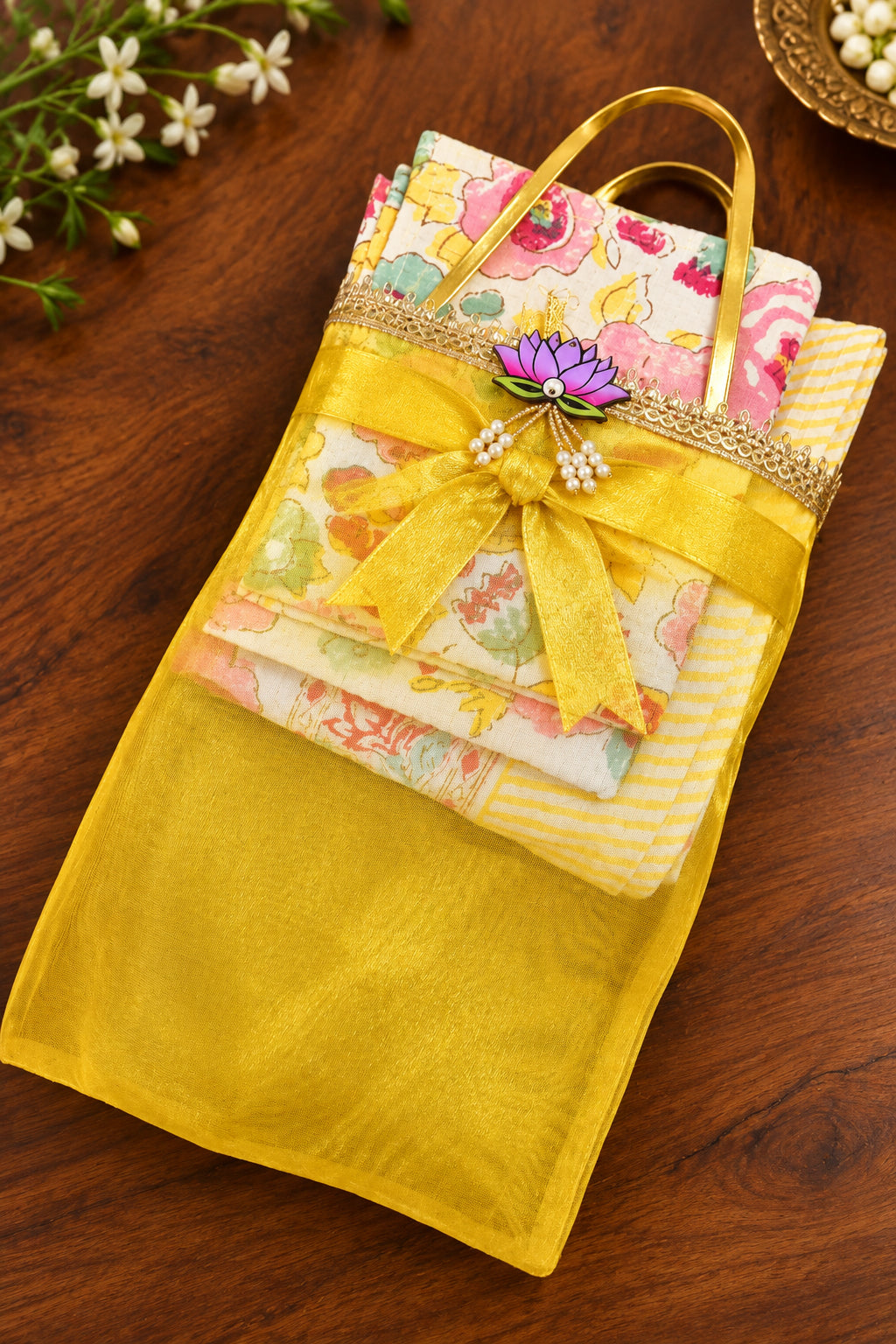 A folded traditional Japanese kimono robe with a yellow mesh cover and gold handles, decorated with a floral brooch and pearl beads, resting on a dark wooden surface.