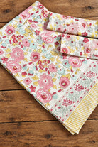 A folded cotton kitchen towel with a colorful floral print and a yellow striped border, displayed on a rustic wooden surface.