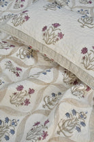 A close-up of a quilted bedding set featuring a cream-colored quilt and matching pillowcase with embroidered floral motifs in muted pink, blue, and beige.