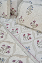A close-up of a quilted bedding set featuring cream-colored fabric with embroidered floral motifs in pink, purple, and blue, accented by striped borders.