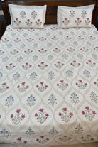 A bedsheet with a cream-colored sheet featuring a repeating floral block print pattern in muted pink, blue, and gray, with two matching pillowcases at the head.