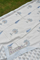 White embroidered fabric with blue floral patterns on a grassy background