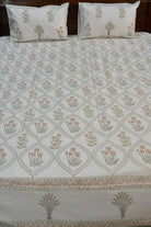 A bed dressed with a white cotton bedsheet featuring a repeating peach and gray floral block print, with two matching pillowcases resting against a dark wooden headboard.
