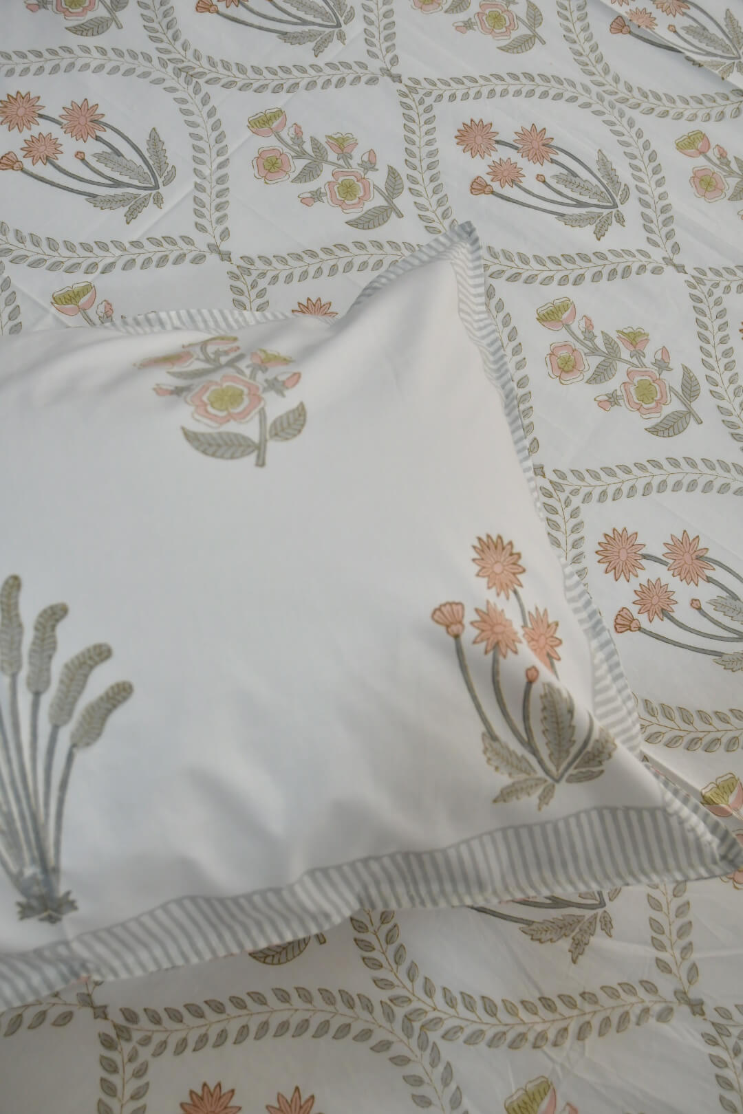 A close-up of a white pillowcase with a delicate floral and botanical block print, layered over a matching patterned bedsheet