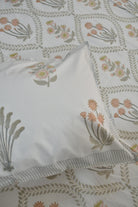 A close-up of a white pillowcase with a delicate floral and botanical block print, layered over a matching patterned bedsheet