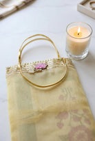 A pale yellow sheer organza handbag with a gold-tone metal handle, decorated with a small pink flower and white pearl embellishment at the top, resting on a dark wooden surface.