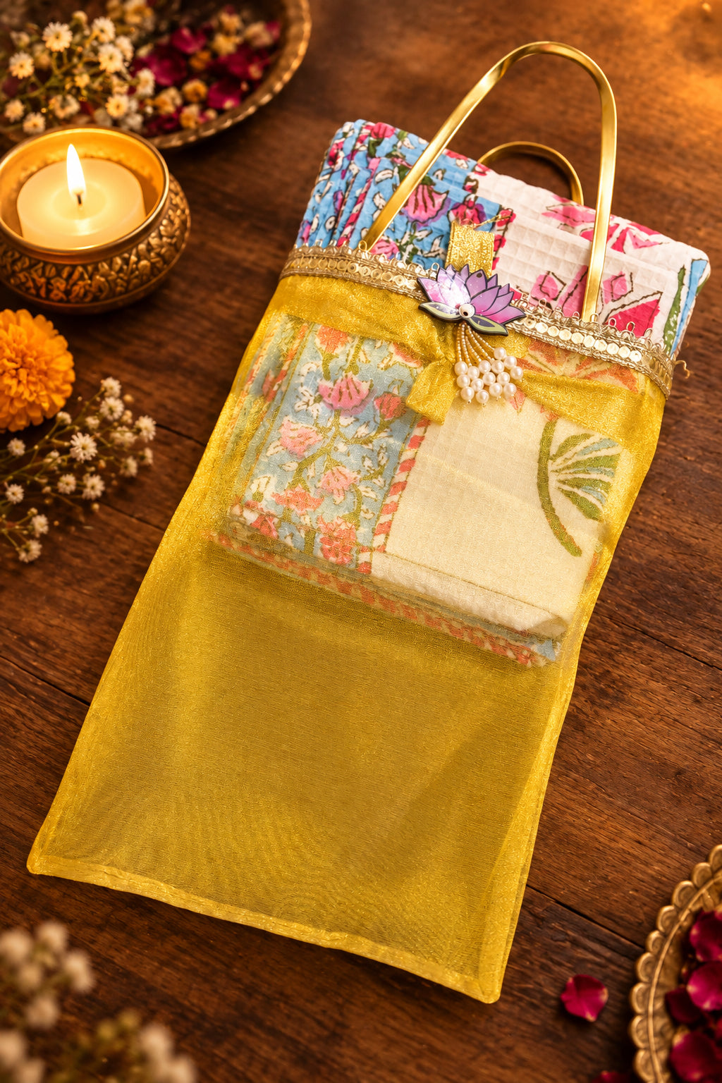A yellow sheer mesh hanging bag with a gold-tone handle, decorated with a floral-patterned fabric panel and a small purple flower embellishment, shown on a dark tabletop.