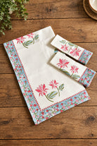 A matching kitchen towel set with a white waffle-weave texture, featuring pink floral motifs and a blue floral border, displayed on a rustic wooden table.