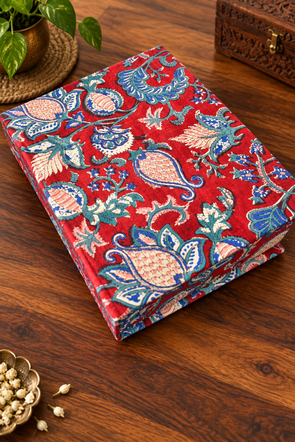 A stack of patterned fabric napkins or table linens with a red base and blue, teal, and beige paisley floral motifs, resting on a dark wooden surface.