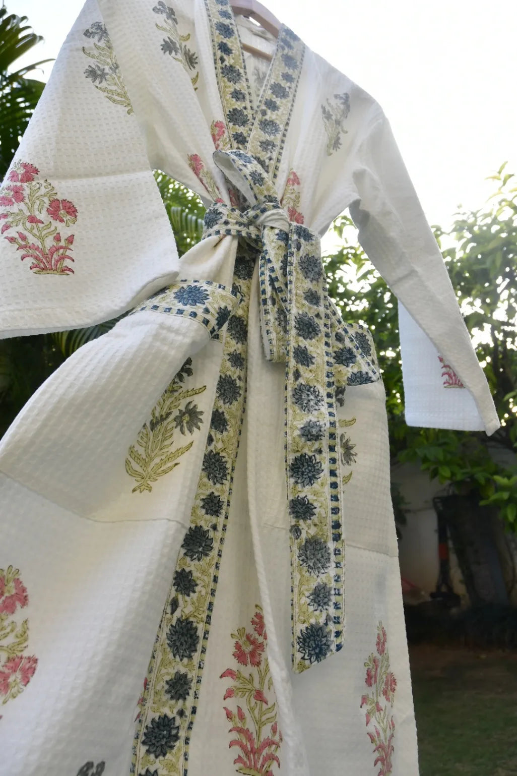 Traditional outfit with floral patterns and a tie, set against a blurred natural background.