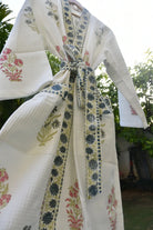 Traditional outfit with floral patterns and a tie, set against a blurred natural background.