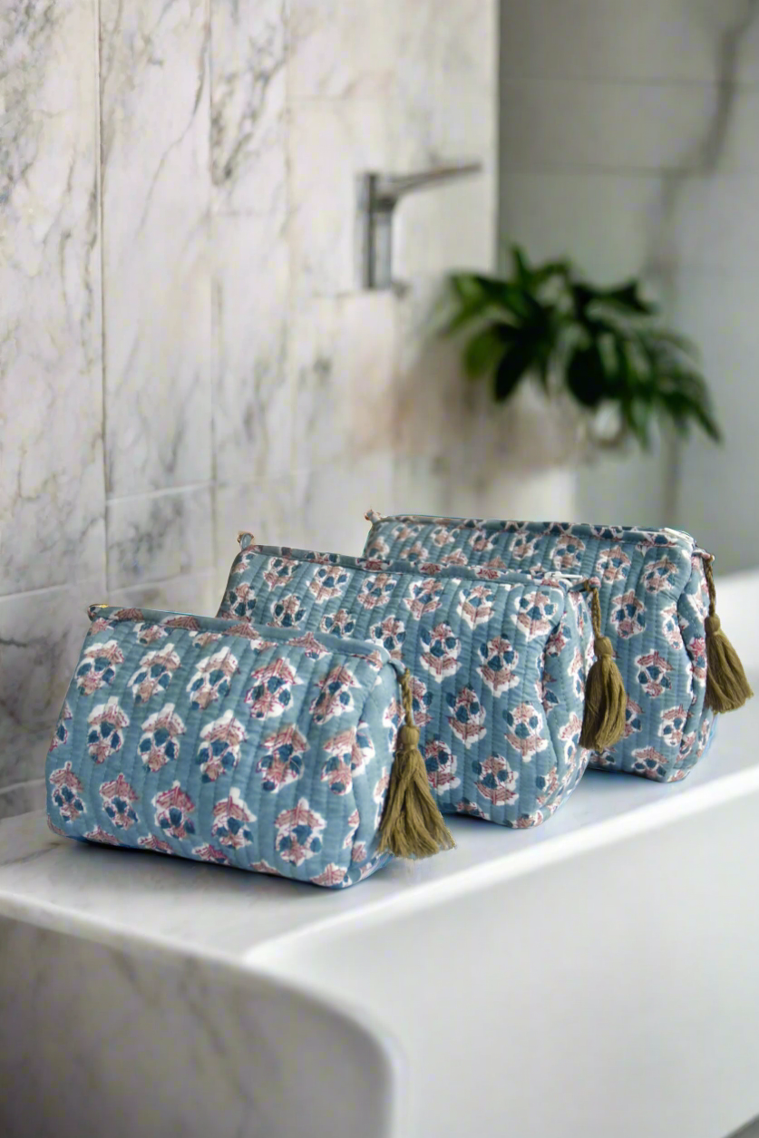 Set of three floral-patterned toiletry bags with tassels on a marble surface.