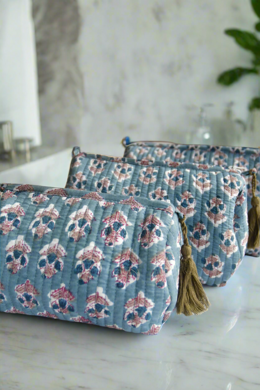 Two blue floral-patterned pouches with tassels on a marble surface.