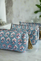 Two blue floral-patterned pouches with tassels on a marble surface.