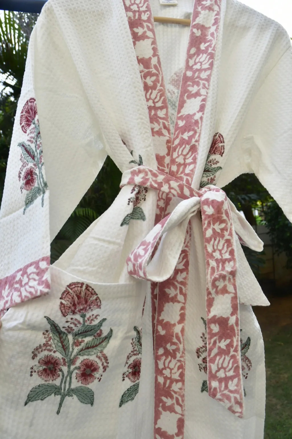 White robe with pink floral patterns and a matching belt against a blurred green background