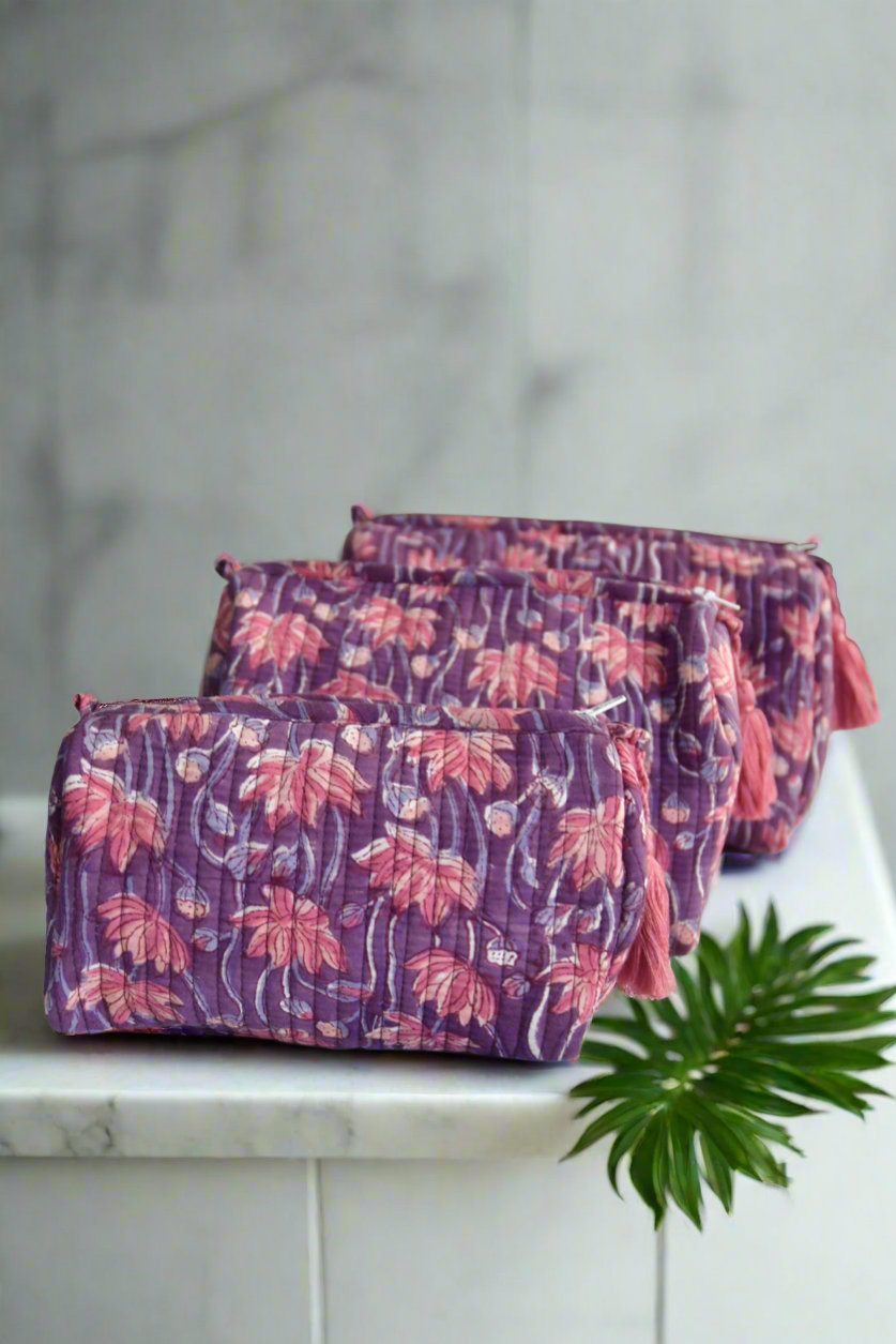 Set of three floral-patterned makeup bags on a marble surface with a plant in the background.