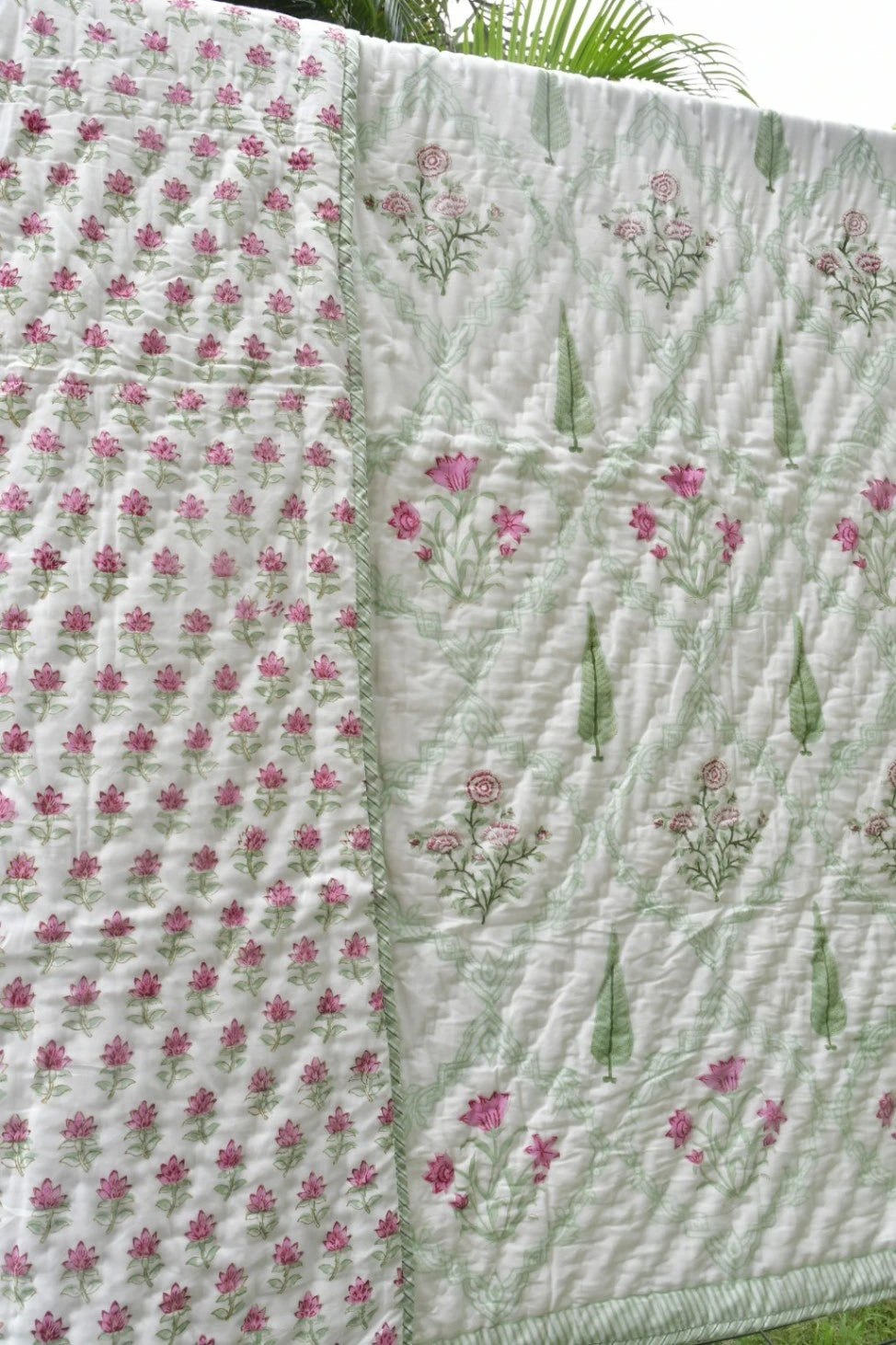 A quilted blanket with a dual-pattern design, featuring one side with small pink flowers on a white background and the other with larger pink floral clusters and green leaves on a light green background.