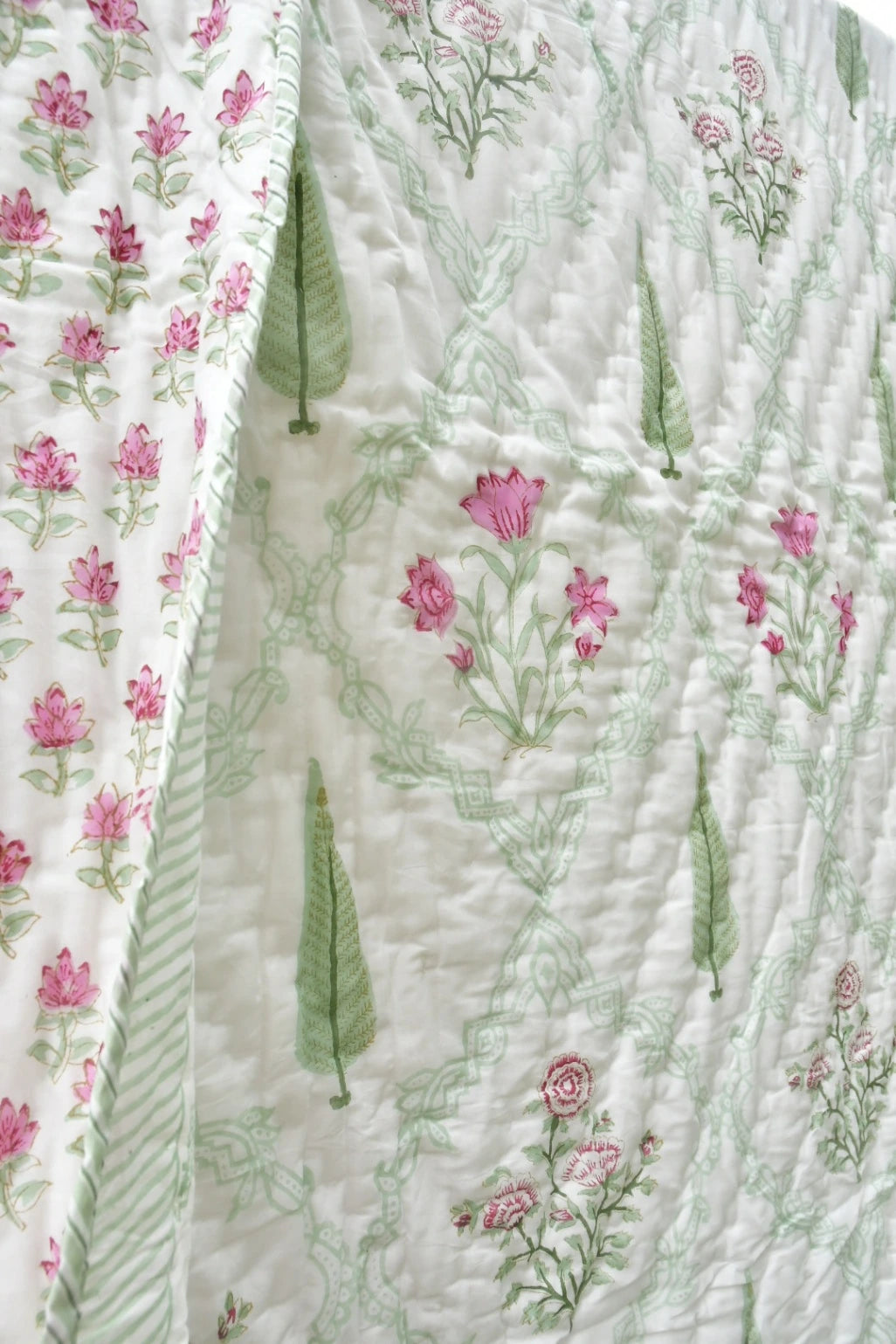 A close-up of a quilted fabric panel featuring a white background with light green botanical line patterns, pink floral motifs, and green leaf shapes. A second adjacent panel shows a repeating pink flower print on a white base.