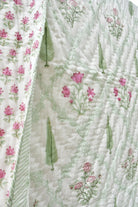 A close-up of a quilted fabric panel featuring a white background with light green botanical line patterns, pink floral motifs, and green leaf shapes. A second adjacent panel shows a repeating pink flower print on a white base.